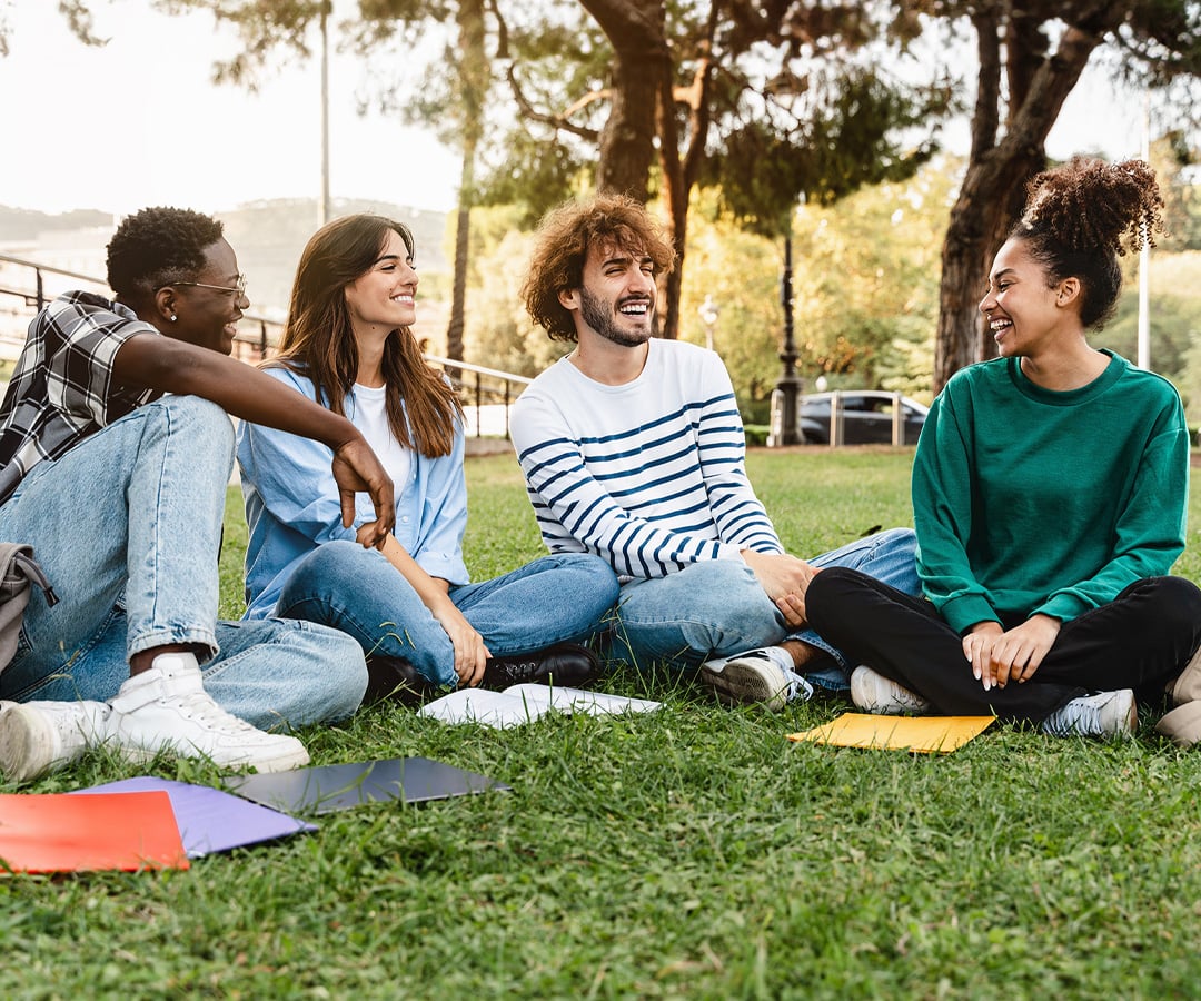 Group of gen Z young adults sitting on grass.